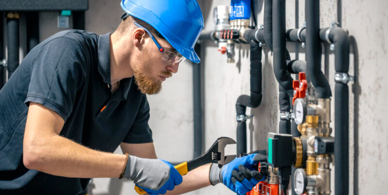 Commercial plumber in hard hat adjusting industrial piping with a wrench