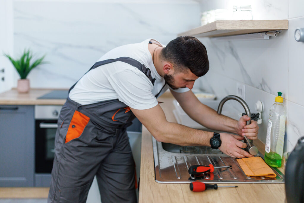 A professional plumber repairing a kitchen faucet using tools in a modern kitchen