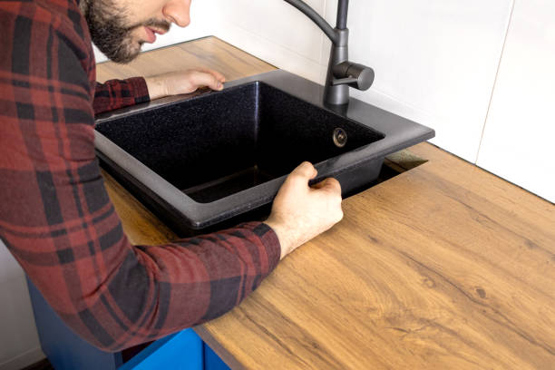Installer securing a black sink into a wooden bar countertop