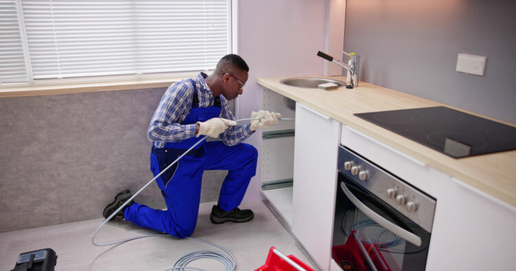 Technician unclogging a kitchen sink drain using a plumbing snake