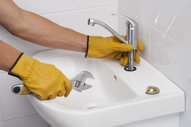 Plumber installing chrome faucet on white bathroom sink with tools