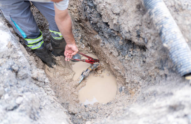 Drain repair contractor working in muddy trench fixing pipes